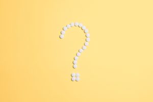 White pills arranged into a question mark shape on a vibrant yellow background.
